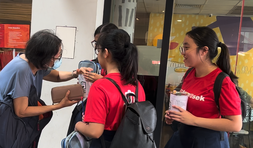 Four young people stand near a McDonald's entrance, two in red shirts, one holding a donation tin.